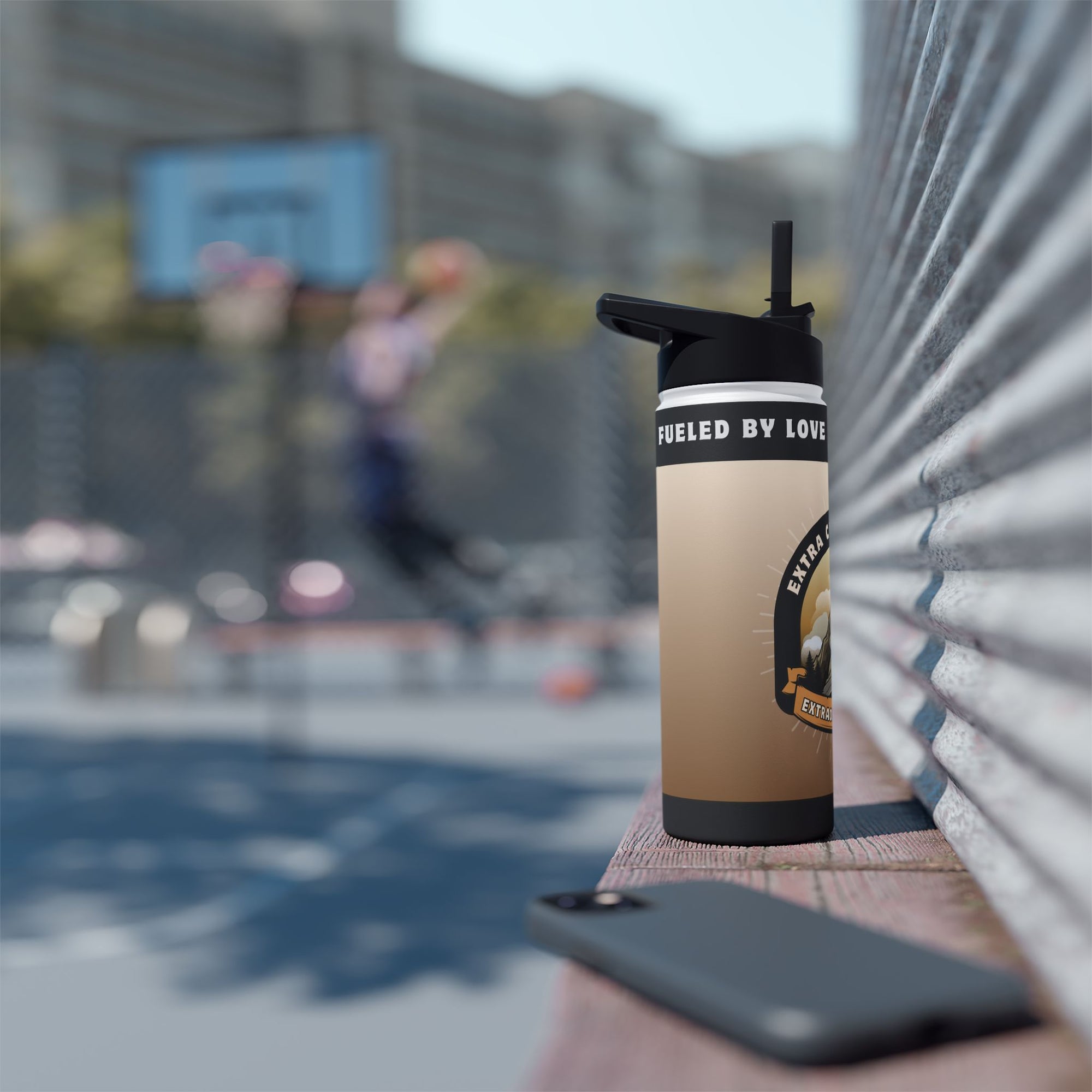Brown tumbler with "Fueled by Love" text rests on a ledge near a basketball court.
